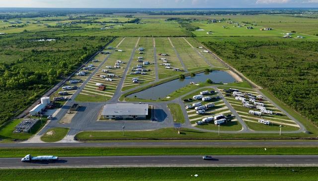 Aerial view of American Dream RV Park with RV rows, pond, and clubhouse beside a highway