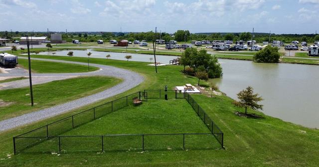 Fenced grassy dog area beside a pond with RVs parked in the background