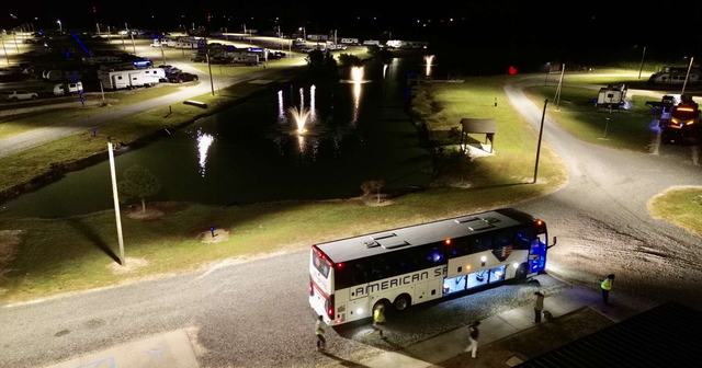 Charter bus parked near a lit pond with fountains at night