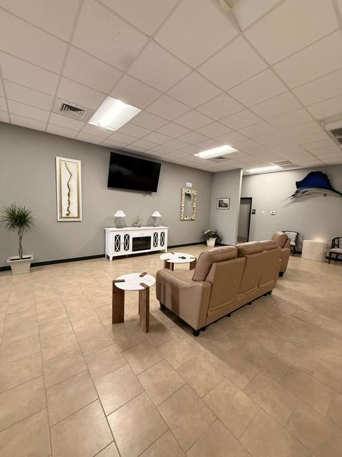 Lounge with tan leather sofa, small tables, wall-mounted TV, and tiled floor