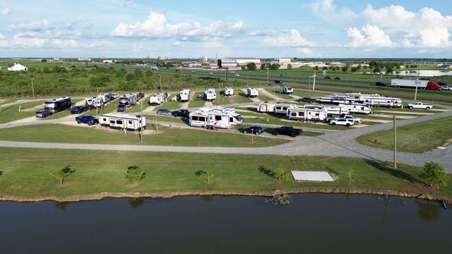 Aerial view of RVs parked along gravel roads beside a pond near a highway
