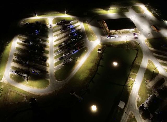 Overhead night view of illuminated RV sites, roads, pond, and main building