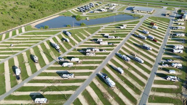 Aerial view of long grassy RV site rows with scattered RVs and a pond