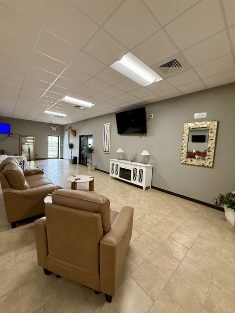 Lounge with tan leather recliners, wall-mounted TV, white cabinet, and decorative mirror