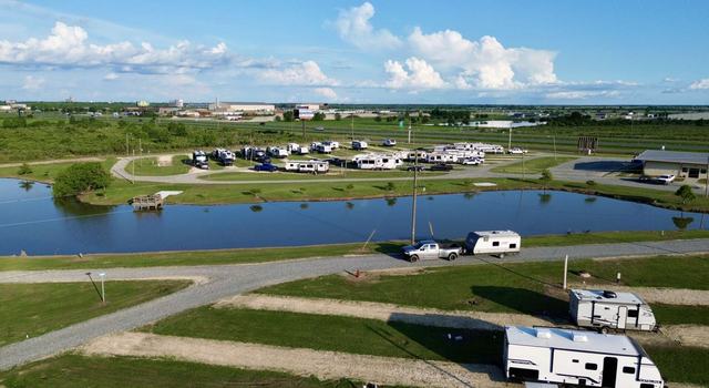 Truck towing a travel trailer on a gravel road beside a pond with RVs