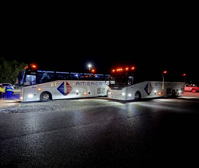Two white charter buses parked at night with workers in safety vests nearby