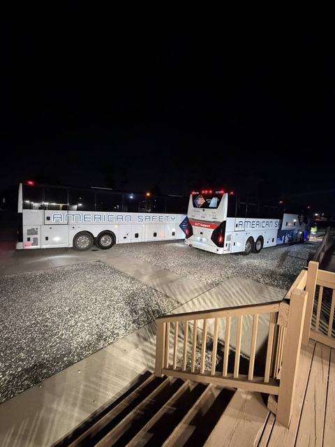 Two white charter buses parked at night viewed from a wooden deck staircase