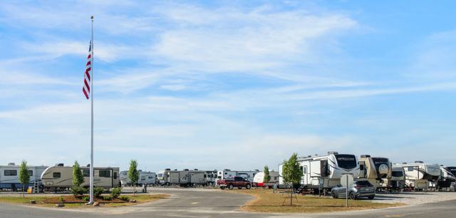 American flag on a tall pole at the entrance to rows of parked RVs