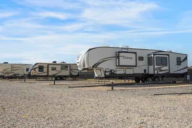Fifth wheel and travel trailers parked on gravel sites under a blue sky