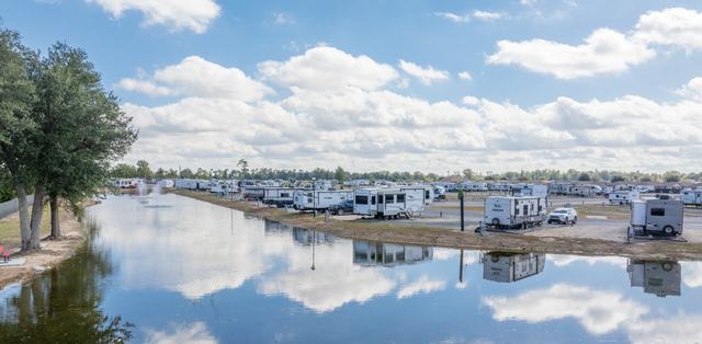 Pond reflecting clouds with RVs parked along its bank and a fountain