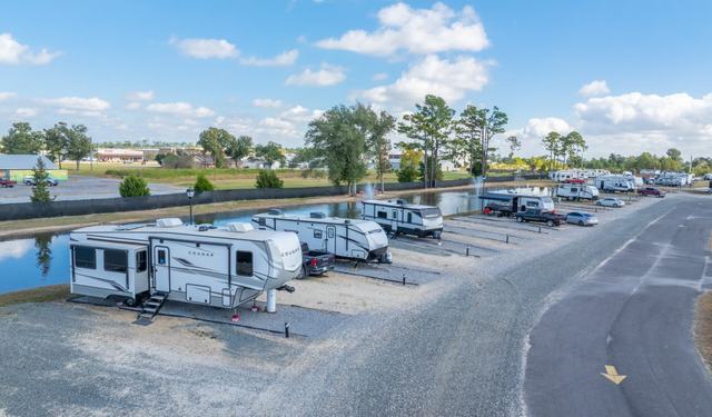 RVs parked on gravel sites along a pond next to a paved road
