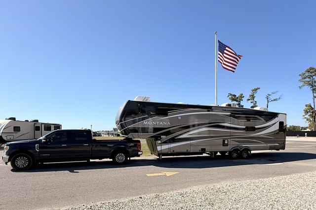 Pickup truck towing a large fifth wheel past a tall American flag
