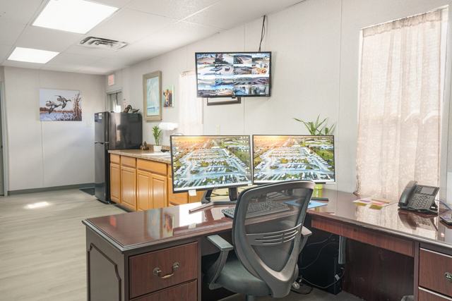 Office desk with two monitors, a security camera screen, and a kitchenette