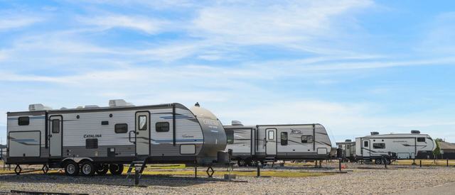 Row of travel trailers parked on gravel sites under a partly cloudy sky