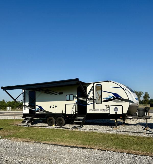 Travel trailer with awning extended parked on a gravel site beside grass
