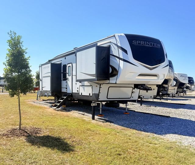 Fifth wheel with slide outs parked on gravel next to a young tree