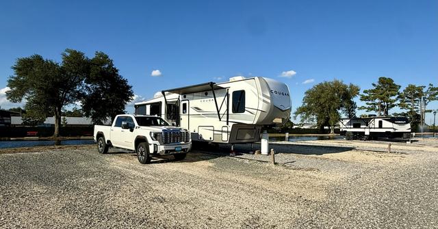 White pickup truck and fifth wheel parked on a gravel site near water