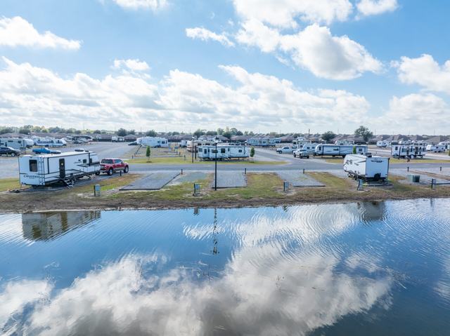 RVs parked along a pond reflecting clouds with homes in the background