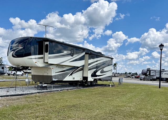 Large fifth wheel parked on a gravel site beside grass and a lamppost