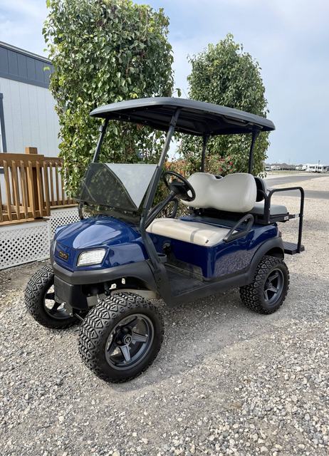 Blue golf cart with rear seat parked on gravel near a building