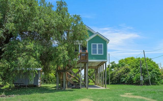Green elevated Pecan Island Camp house on stilts beside a large oak tree