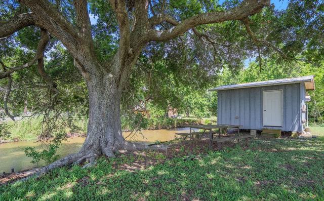 Large oak tree with picnic table and gray shed beside a small waterway