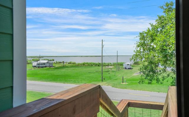 Porch view across a road toward grassy lots, campers, and open water