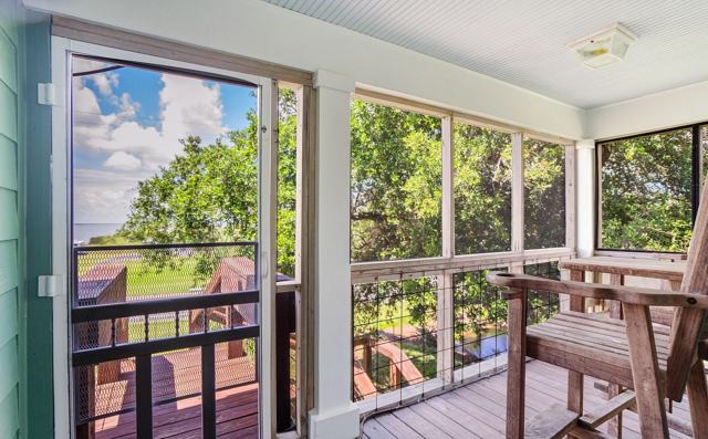 Screened porch with wooden chair and door leading out to a deck
