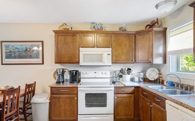 Kitchen with wood cabinets, white electric stove, microwave, and double sink