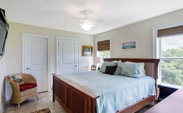 Bedroom with wooden king bed, ceiling fan, wicker chair, and two doors