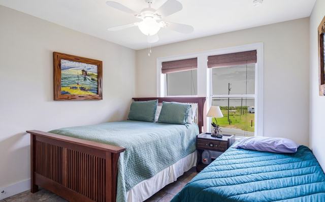 Bedroom with wooden bed, single bed, ceiling fan, and window overlooking road