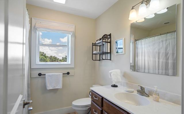 Bathroom with white vanity, mirror, toilet, window, and shower curtain