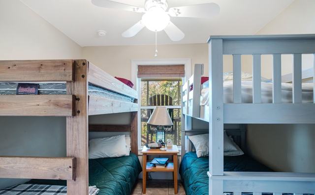 Bunk room with two bunk beds, nightstand with lamp, and ceiling fan