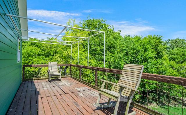 Wooden deck with metal frame overhead, two rocking chairs, and green trees