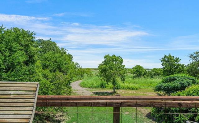 Deck view over railing toward a gravel path, trees, and open marshland