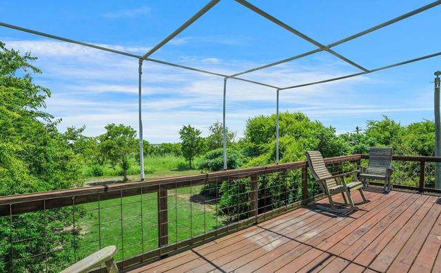 Wooden deck with metal canopy frame, rocking chairs, and views of greenery