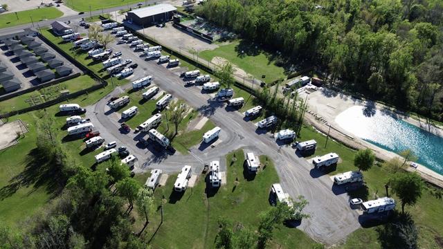 Aerial view of Rustic Oak RV Park with rows of RVs beside a pond and woods