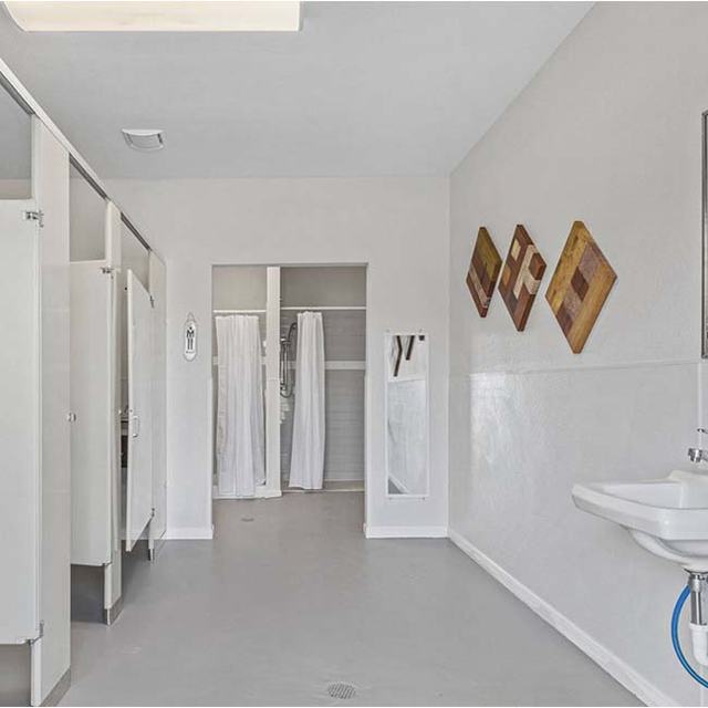 Restroom with toilet stalls, a wall sink, wooden wall art and showers beyond