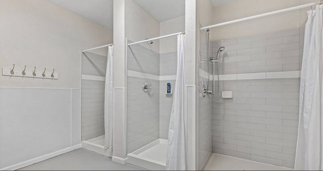 Row of tiled shower stalls with white curtains and wall hooks
