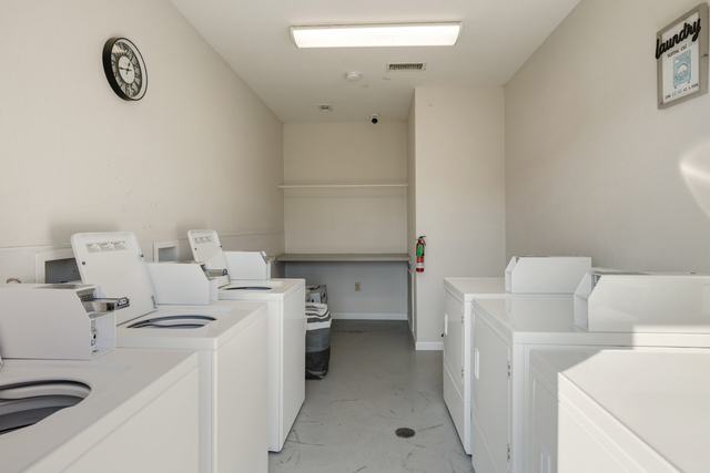 Laundry room with rows of white washers and dryers and a wall clock