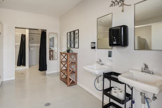 Restroom with two wall sinks, mirrors, wooden shelf and a shower area