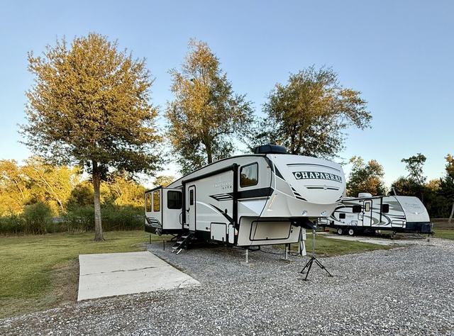 Fifth wheel trailer parked on a gravel site beside a concrete pad and trees
