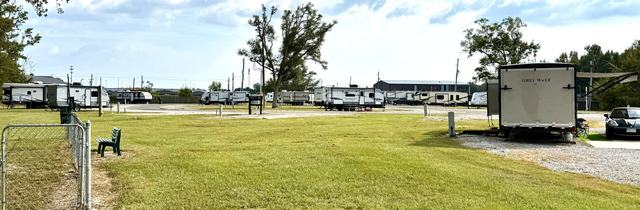 Grassy lawn with a bench and fence beside rows of parked RVs