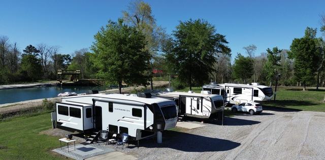 RVs parked on gravel sites beside trees and a waterway